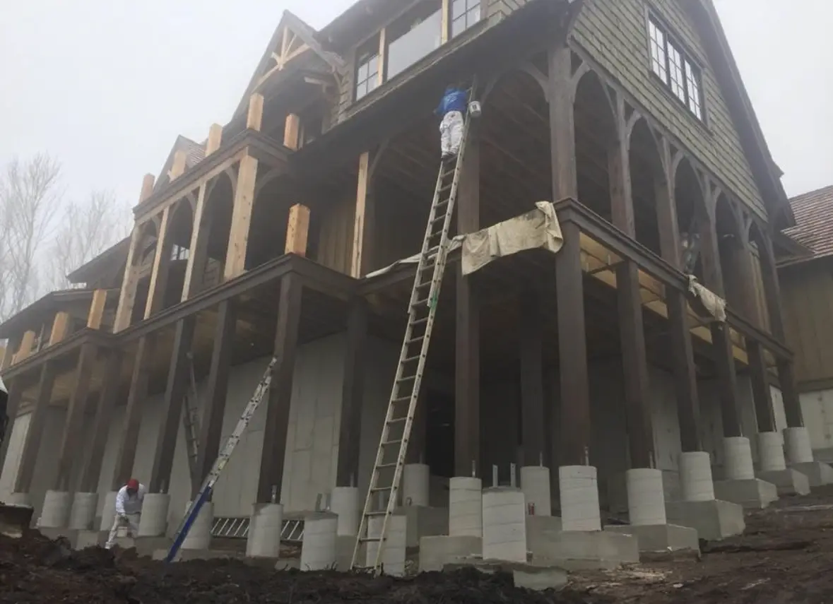 Painter on a tall ladder coating timber columns and porch beams on a new lodge