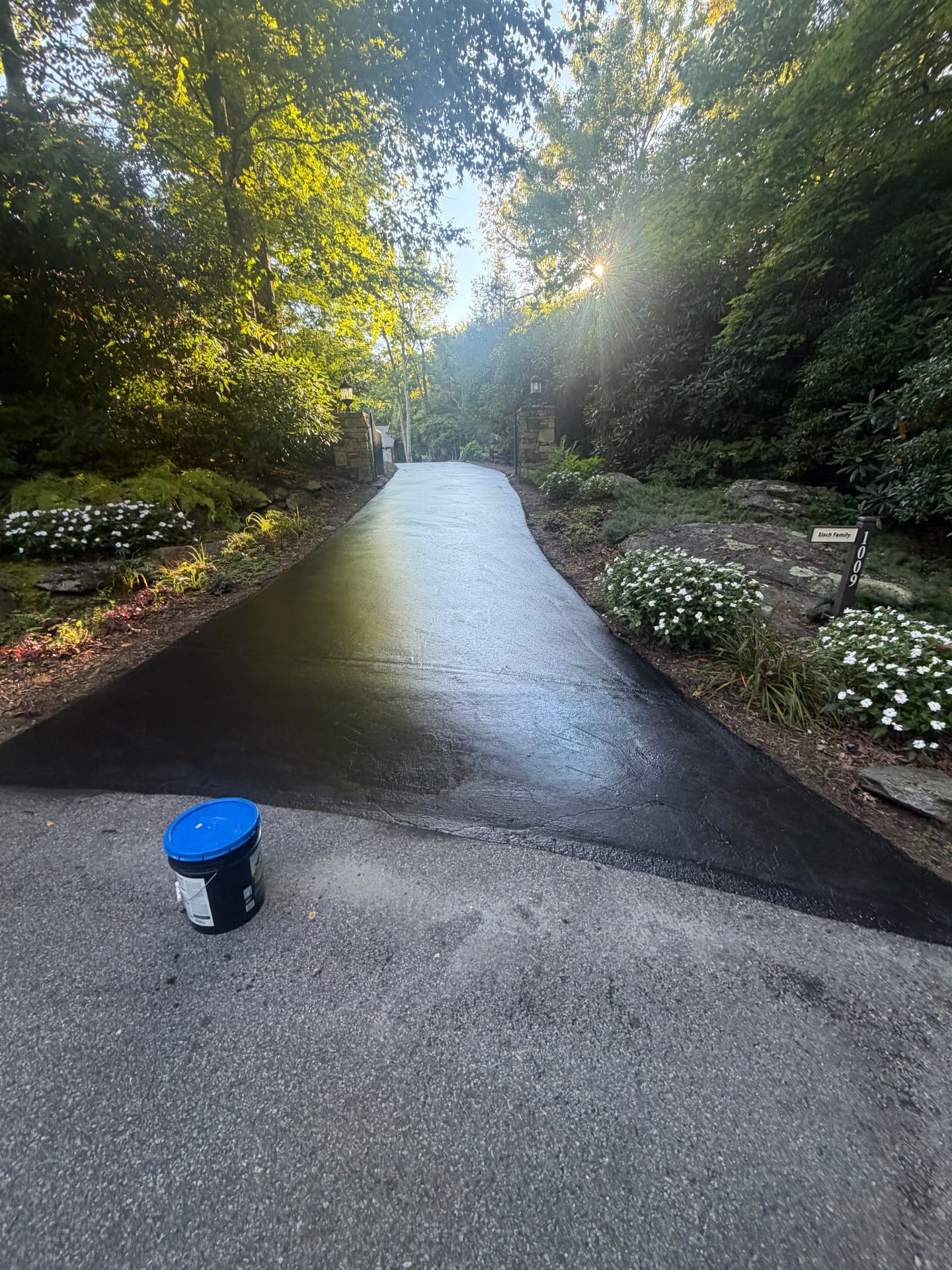 Driveway entrance freshly sealcoated glossy black with the sealer bucket in front