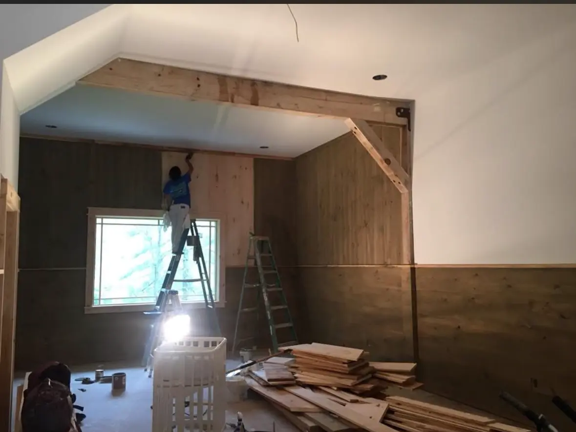 Painter on a ladder cutting in pine paneling and white ceilings in a timber frame room
