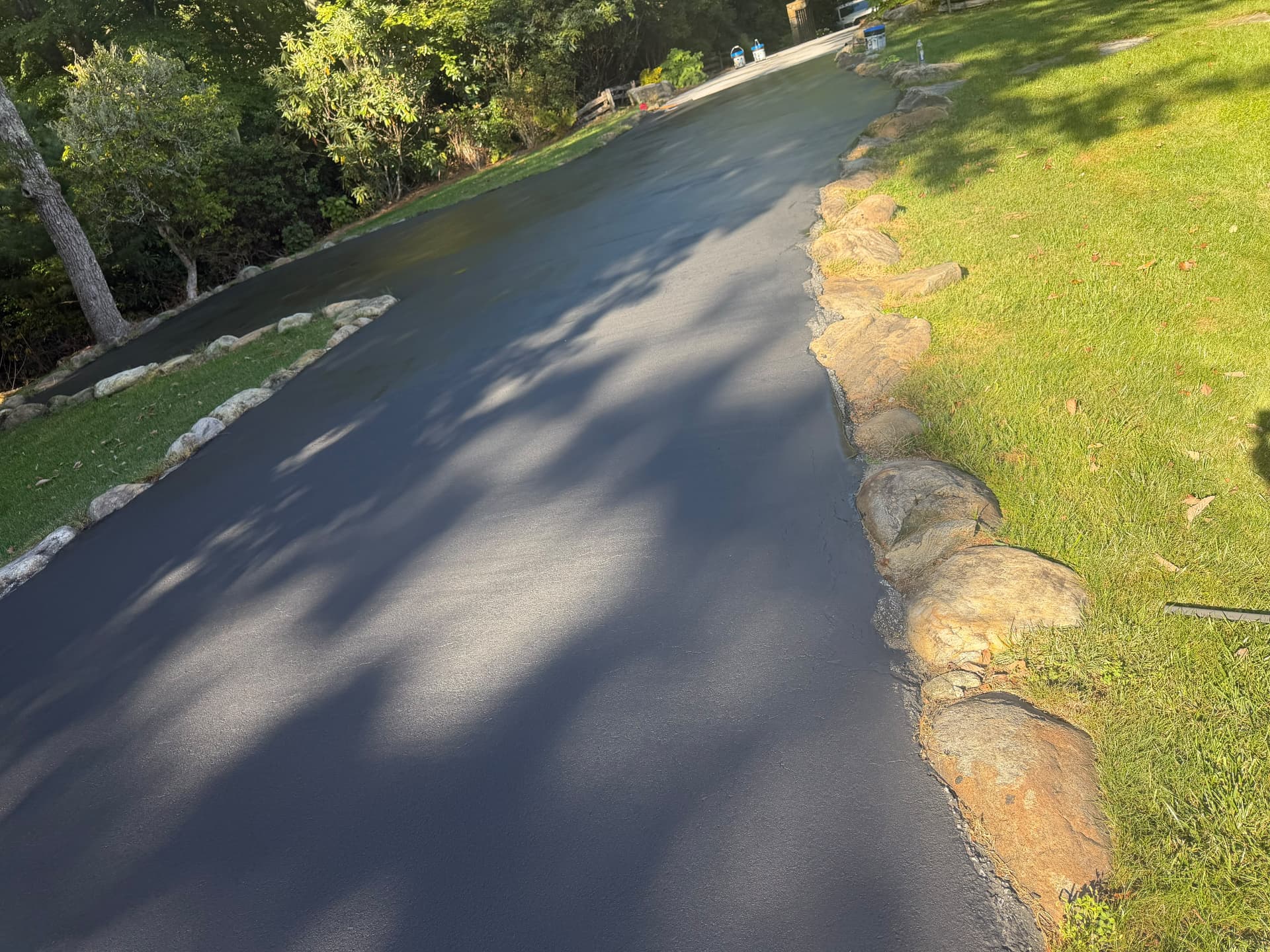 Wide driveway sealcoated deep black along large stone edging in full sun