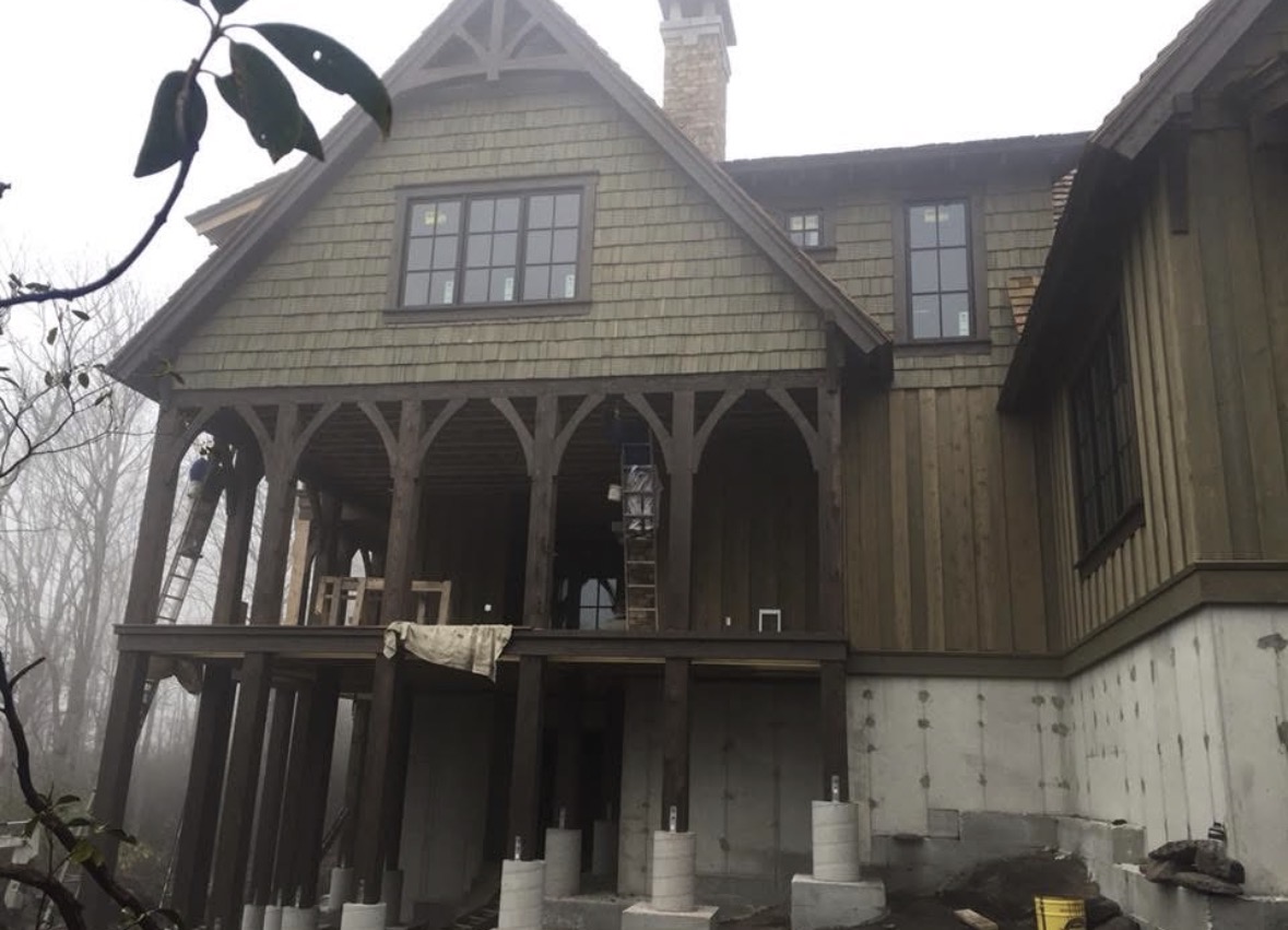 Covered timber frame porch with arched beams stained dark brown under shake siding