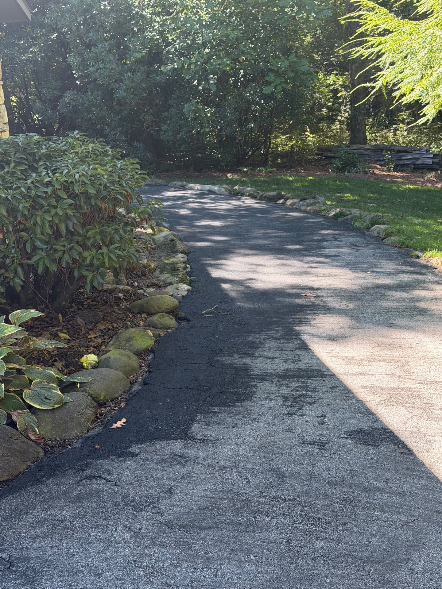 Curved front walkway freshly sealcoated black next to landscaping stone borders